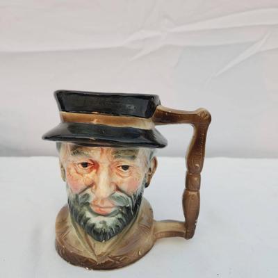 Sale Photo Thumbnail #229: A three-piece set including a Homer Laughlin Virginia Rose plate (Made in USA, pattern C48N8), a teapot with mark 'Made in England,' and a ceramic figurative mug resembling a bearded man wearing a hat. The plate features a floral design with scalloped edg