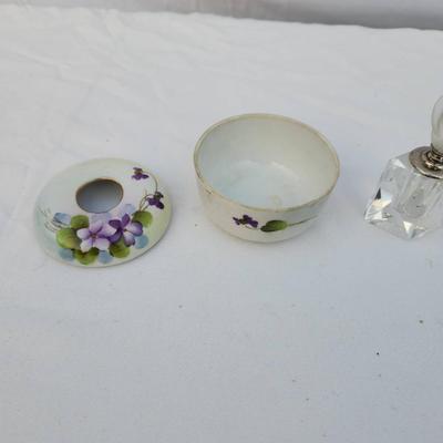 Sale Photo Thumbnail #232: Includes a circular hand-painted porcelain trinket box with floral violet designs and a brass-rimmed opening, accompanied by a small clear crystal perfume bottle with a frosted glass stopper in a floral shape. Both items are in acceptable condition with s