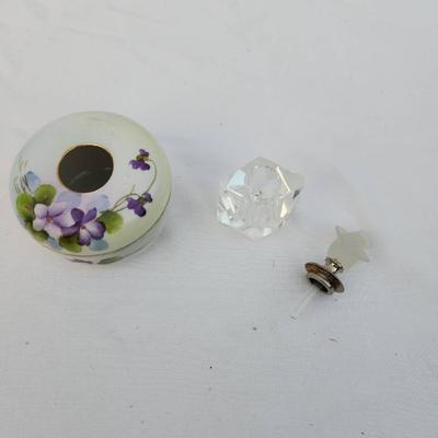 Sale Photo Thumbnail #231: Includes a circular hand-painted porcelain trinket box with floral violet designs and a brass-rimmed opening, accompanied by a small clear crystal perfume bottle with a frosted glass stopper in a floral shape. Both items are in acceptable condition with s
