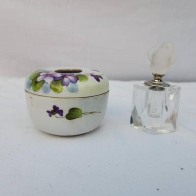 Sale Photo Thumbnail #230: Includes a circular hand-painted porcelain trinket box with floral violet designs and a brass-rimmed opening, accompanied by a small clear crystal perfume bottle with a frosted glass stopper in a floral shape. Both items are in acceptable condition with s