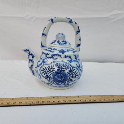 Sale Photo Thumbnail #235: A ceramic teapot featuring a blue and white floral design and a handle at the top. The bottom is marked 'Made in China.' The teapot has a removable lid and appears to be medium in size with measurements evident against the included ruler.