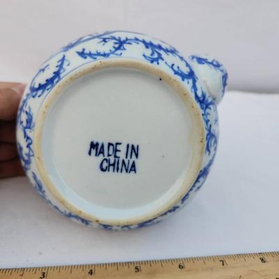 Sale Photo Thumbnail #237: A ceramic teapot featuring a blue and white floral design and a handle at the top. The bottom is marked 'Made in China.' The teapot has a removable lid and appears to be medium in size with measurements evident against the included ruler.
