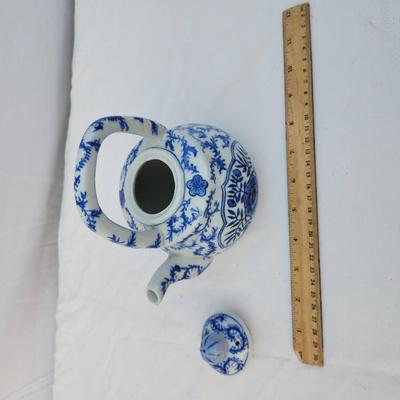 Sale Photo Thumbnail #236: A ceramic teapot featuring a blue and white floral design and a handle at the top. The bottom is marked 'Made in China.' The teapot has a removable lid and appears to be medium in size with measurements evident against the included ruler.