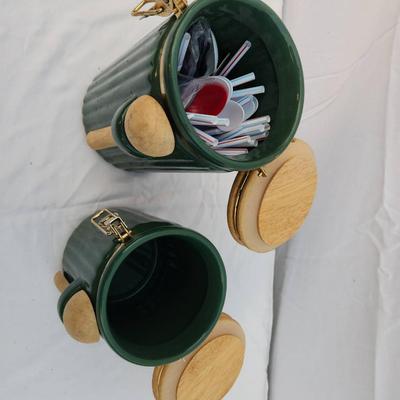 Sale Photo Thumbnail #239: Two ribbed ceramic canisters in a green finish, featuring hinged wooden lids and matching wooden spoons secured on the fronts. Each canister is fitted with a clasp closure to ensure a tight seal. These functional and decorative items are suitable for hold