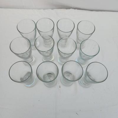 Sale Photo Thumbnail #243: 10 identical clear glass tumbler-style glasses with a curved design and slightly flared rim. Each glass features a weighted base for stability. Great for serving beverages. All glasses are in good condition with no visible chips or cracks.