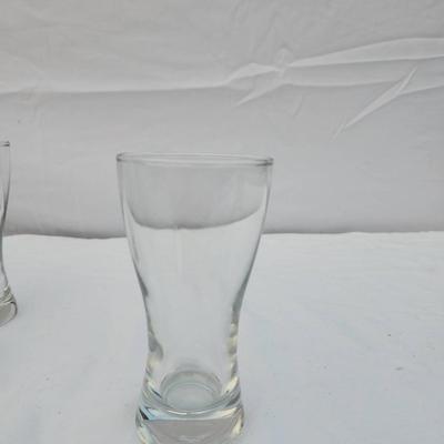 Sale Photo Thumbnail #242: 10 identical clear glass tumbler-style glasses with a curved design and slightly flared rim. Each glass features a weighted base for stability. Great for serving beverages. All glasses are in good condition with no visible chips or cracks.