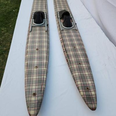 Sale Photo Thumbnail #261: Vintage water skis crafted from wood, featuring a distinctive plaid pattern on the surface. The skis are equipped with metal bindings and black foot straps. Visible wear is present, including scratches and marks consistent with use and age. The underside 