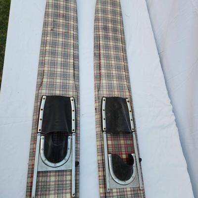 Sale Photo Thumbnail #260: Vintage water skis crafted from wood, featuring a distinctive plaid pattern on the surface. The skis are equipped with metal bindings and black foot straps. Visible wear is present, including scratches and marks consistent with use and age. The underside 