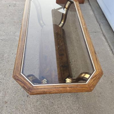 Sale Photo Thumbnail #296: Rectangular glass-top coffee table featuring an octagonal beveled edge and a solid wood frame with a rich finish. The base showcases brass accents and a wood lower shelf with a decorative veneer. Sturdy construction combines materials for a sophisticated 