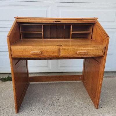 Sale Photo Thumbnail #297: Oak roll-top desk featuring a tambour front that slides open to reveal storage compartments and cubbyholes. Includes two pull-out drawers beneath the desktop for additional storage. The desk showcases a natural wood grain finish and paneled sides. Ideal f