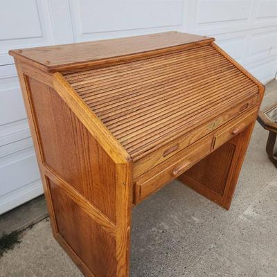 Sale Photo Thumbnail #301: Oak roll-top desk featuring a tambour front that slides open to reveal storage compartments and cubbyholes. Includes two pull-out drawers beneath the desktop for additional storage. The desk showcases a natural wood grain finish and paneled sides. Ideal f
