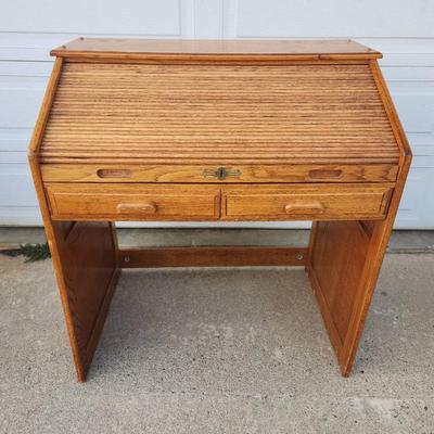 Sale Photo Thumbnail #300: Oak roll-top desk featuring a tambour front that slides open to reveal storage compartments and cubbyholes. Includes two pull-out drawers beneath the desktop for additional storage. The desk showcases a natural wood grain finish and paneled sides. Ideal f