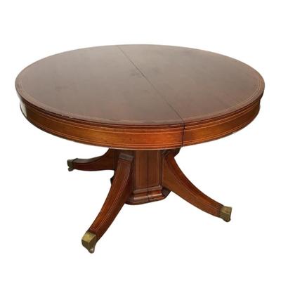 Sale Photo Thumbnail #1593: This magnificent round dining table, crafted from rich mahogany, offers both elegance and versatility for any dining space. The tabletop showcases a beautifully executed striped inlay design radiating from the center, adding a touch of refined detail and 