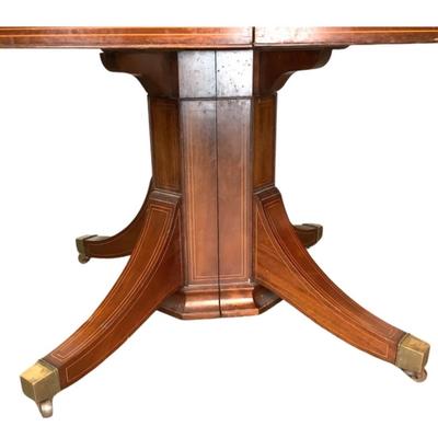 Sale Photo Thumbnail #1596: This magnificent round dining table, crafted from rich mahogany, offers both elegance and versatility for any dining space. The tabletop showcases a beautifully executed striped inlay design radiating from the center, adding a touch of refined detail and 