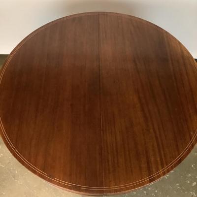 Sale Photo Thumbnail #1604: This magnificent round dining table, crafted from rich mahogany, offers both elegance and versatility for any dining space. The tabletop showcases a beautifully executed striped inlay design radiating from the center, adding a touch of refined detail and 