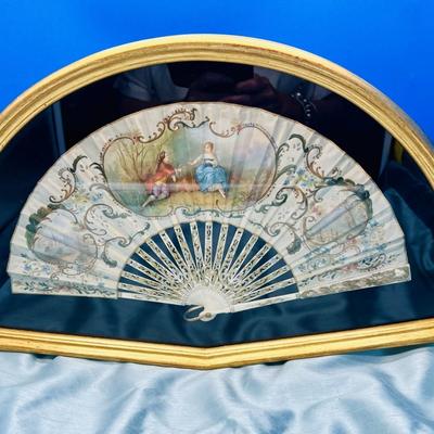 Sale Photo Thumbnail #398: A folding hand fan, antique, in a shadow box frame   Mother of pearl on the  sticks with the scene likely painted on silk or similar material. The sticks are likely bone, carved and pierced.  Signed by Lucien. Shadow box is 20 3/4 x 12 inches.  
Retails a