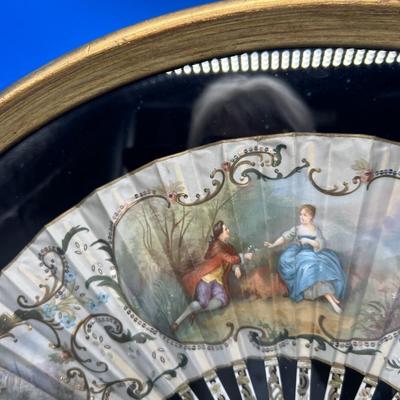 Sale Photo Thumbnail #399: A folding hand fan, antique, in a shadow box frame   Mother of pearl on the  sticks with the scene likely painted on silk or similar material. The sticks are likely bone, carved and pierced.  Signed by Lucien. Shadow box is 20 3/4 x 12 inches.  
Retails a
