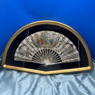 Sale Photo Thumbnail #400: A folding hand fan, antique, in a shadow box frame   Mother of pearl on the  sticks with the scene likely painted on silk or similar material. The sticks are likely bone, carved and pierced.  Signed by Lucien. Shadow box is 20 3/4 x 12 inches.  
Retails a