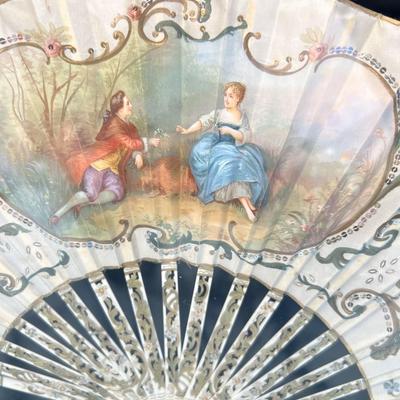 Sale Photo Thumbnail #396: A folding hand fan, antique, in a shadow box frame   Mother of pearl on the  sticks with the scene likely painted on silk or similar material. The sticks are likely bone, carved and pierced.  Signed by Lucien. Shadow box is 20 3/4 x 12 inches.  
Retails a