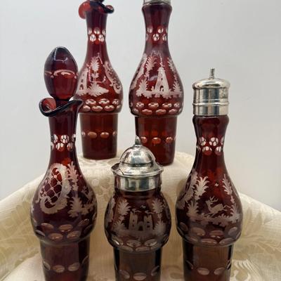 Sale Photo Thumbnail #423: From late 19th or early 20th Century, 5 ruby red glass bottles with 'cut to clear' etchings of trees, buildings, and deer.  
Held in silver plate stand, which needs polishing.  Bottles are for oil, vinegar, salt, pepper, and mustard.
13 inches tall with s