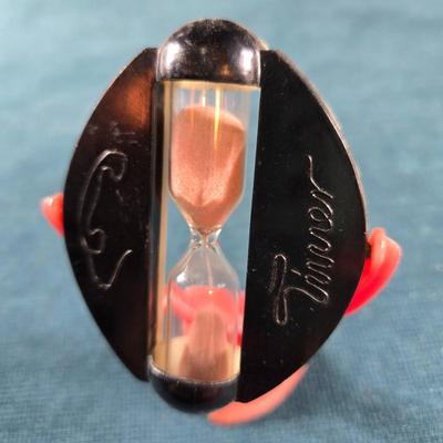 Sale Photo Thumbnail #133: This  auction lot is for a West German Timer, Thiis a vintage West German Timer.  It times for 3 minutes.  It is in overall good condition but the red plastic stand shows some fading. The holder and stand are plastic but the hour glass is glass.  It is ab