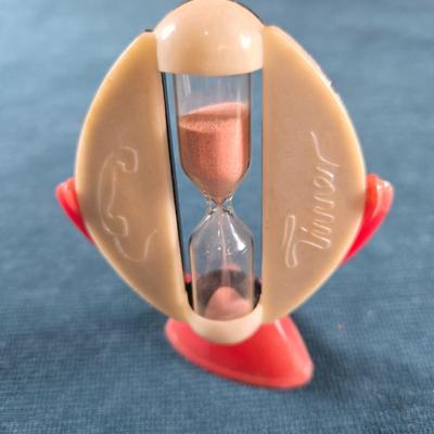 Sale Photo Thumbnail #134: This  auction lot is for a West German Timer, Thiis a vintage West German Timer.  It times for 3 minutes.  It is in overall good condition but the red plastic stand shows some fading. The holder and stand are plastic but the hour glass is glass.  It is ab
