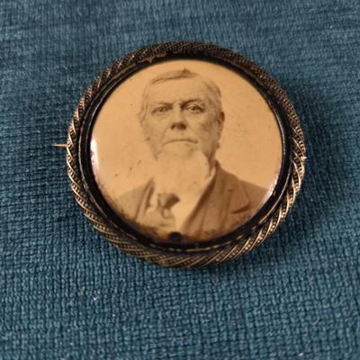 Sale Photo Thumbnail #180: This auction lot is for a Victorian Mourning Broach - #2. This is a Victorian Mourning Broach of an older man.  It is encased in what we think is silver plate that is nicely tarnished with a glass cover.  It is about 1-3/8-inches in diameter.  It is in ve
