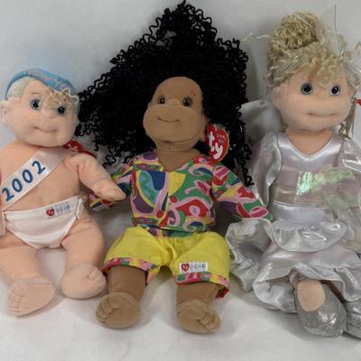Sale Photo Thumbnail #136: The doll on the left is a "New Year 2002" Beanie Kid, wearing a diaper with "2002" written on a sash. 
The doll in the center is named Calypso, and she has black curly hair and is wearing a colorful shirt and yellow shorts. 
The doll on the right is aname