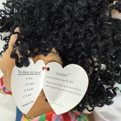 Sale Photo Thumbnail #133: The doll on the left is a "New Year 2002" Beanie Kid, wearing a diaper with "2002" written on a sash. 
The doll in the center is named Calypso, and she has black curly hair and is wearing a colorful shirt and yellow shorts. 
The doll on the right is aname