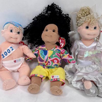 Sale Photo Thumbnail #137: The doll on the left is a "New Year 2002" Beanie Kid, wearing a diaper with "2002" written on a sash. 
The doll in the center is named Calypso, and she has black curly hair and is wearing a colorful shirt and yellow shorts. 
The doll on the right is aname