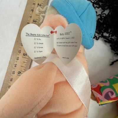 Sale Photo Thumbnail #134: The doll on the left is a "New Year 2002" Beanie Kid, wearing a diaper with "2002" written on a sash. 
The doll in the center is named Calypso, and she has black curly hair and is wearing a colorful shirt and yellow shorts. 
The doll on the right is aname