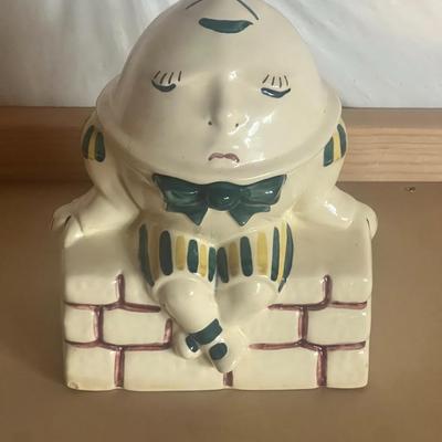 Sale Photo Thumbnail #4: Charming vintage Humpty Dumpty cookie jar, featuring the classic nursery rhyme character sitting on a brick wall. Hand-painted ceramic with soft pastel tones, green bowtie, and striped outfit. Two-piece design with removable head lid.
Perfect for vintage 