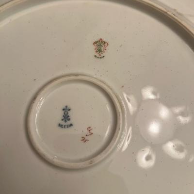 Sale Photo Thumbnail #23: Beautiful antique Ohme Silesia porcelain plate featuring soft blush and ivory roses with a delicate embossed border and gilt accents.
Backstamps include the Ohme Silesia green shield and blue crown Silesia marks, used between 1892–1918. A fine example o