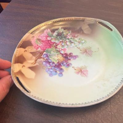 Sale Photo Thumbnail #52: Charming pair of early 20th-century German porcelain serving plates featuring hand-painted florals and grapevine motifs with gold trim.
Includes:
1️⃣ Porcelain handled tray with purple grape cluster design – marked “Jäger & Co Bavaria Germany,”