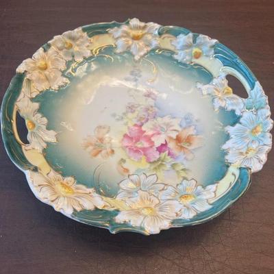 Sale Photo Thumbnail #59: Exquisite antique porcelain handled plate, featuring raised dogwood flower reliefs, teal and cream ombré glaze, and a hand-painted floral center. Edged with gold accents typical of RS Prussia and Reinhold Schlegelmilch styles, this piece dates to the ear