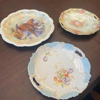 Sale Photo Thumbnail #66: Beautiful trio of early 20th-century European porcelain display plates, each showcasing hand-painted or transfer-decorated artistry and fine embossed detailing.
Included:
1.	Game Bird Plate – embossed rim with scalloped edges, featuring a detailed pheas