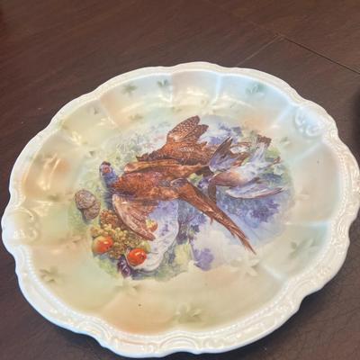 Sale Photo Thumbnail #62: Beautiful trio of early 20th-century European porcelain display plates, each showcasing hand-painted or transfer-decorated artistry and fine embossed detailing.
Included:
1.	Game Bird Plate – embossed rim with scalloped edges, featuring a detailed pheas