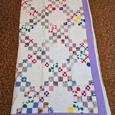 Handmade patchwork quilt featuring a scrappy nine-patch block design and a light purple border. Postage Stamp quilt Irish Chain pattern