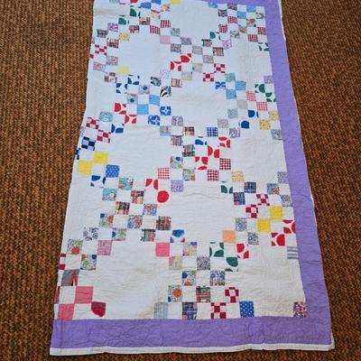 Handmade patchwork quilt featuring a scrappy nine-patch block design and a light purple border. Postage Stamp quilt Irish Chain pattern