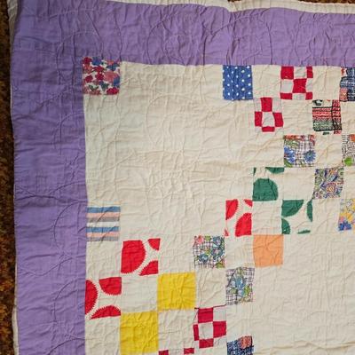 Handmade patchwork quilt featuring a scrappy nine-patch block design and a light purple border. Postage Stamp quilt Irish Chain pattern