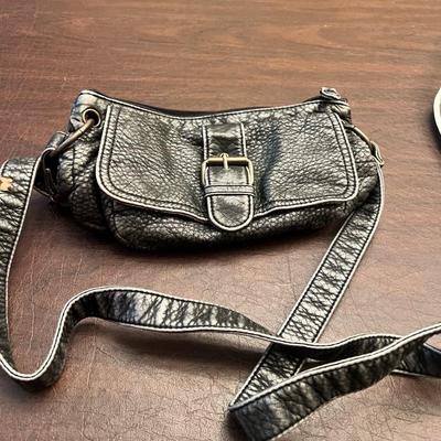 Sale Photo Thumbnail #151: Cute and compact Mudd brand crossbody purse featuring a black pebbled faux-leather exterior with a front buckle-detail pocket. The interior is clean, lined in brown fabric, and includes a zippered accessory pocket. Slim strap makes it perfect for hands-fr