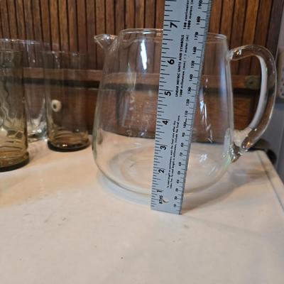 Two glass water pitchers and an assortment of miss-matched drinking glasses