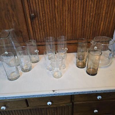 Two glass water pitchers and an assortment of miss-matched drinking glasses