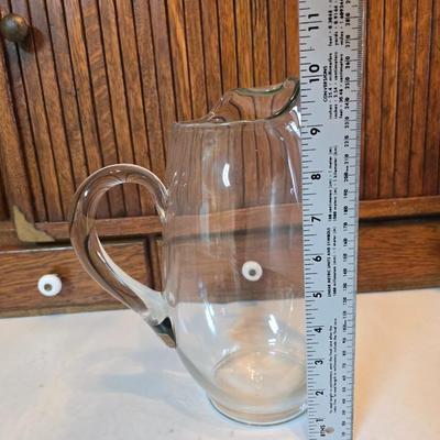 Two glass water pitchers and an assortment of miss-matched drinking glasses