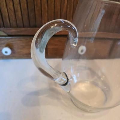 Two glass water pitchers and an assortment of miss-matched drinking glasses