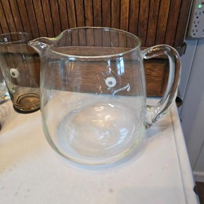 Two glass water pitchers and an assortment of miss-matched drinking glasses