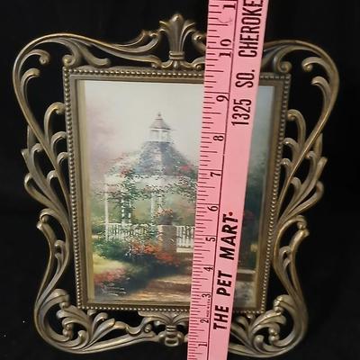 Framed print of the painting "The Hidden Gazebo" by Thomas Kinkade - Two ornate brass picture frames featuring a floral still...