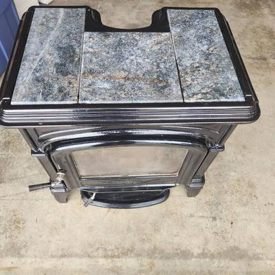Sale Photo Thumbnail #2: Hearthstone cast iron wood-burning stove featuring decorative soapstone panels. The stove has a viewing window on the front door, a top-loading soapstone panel design, and is freestanding. Designed for efficient heating and aesthetic appeal with intricate
