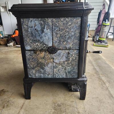 Sale Photo Thumbnail #3: Hearthstone cast iron wood-burning stove featuring decorative soapstone panels. The stove has a viewing window on the front door, a top-loading soapstone panel design, and is freestanding. Designed for efficient heating and aesthetic appeal with intricate