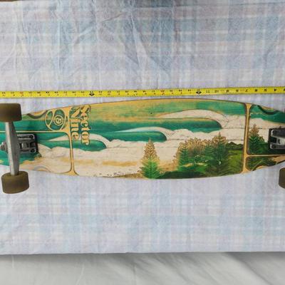 Sale Photo Thumbnail #10: Sector Nine longboard skateboard featuring a wooden deck with a worn graphic design on the underside, painted in green and white with landscape imagery. The board is equipped with trucks and translucent wheels. Some wear is visible on the deck and wheels,
